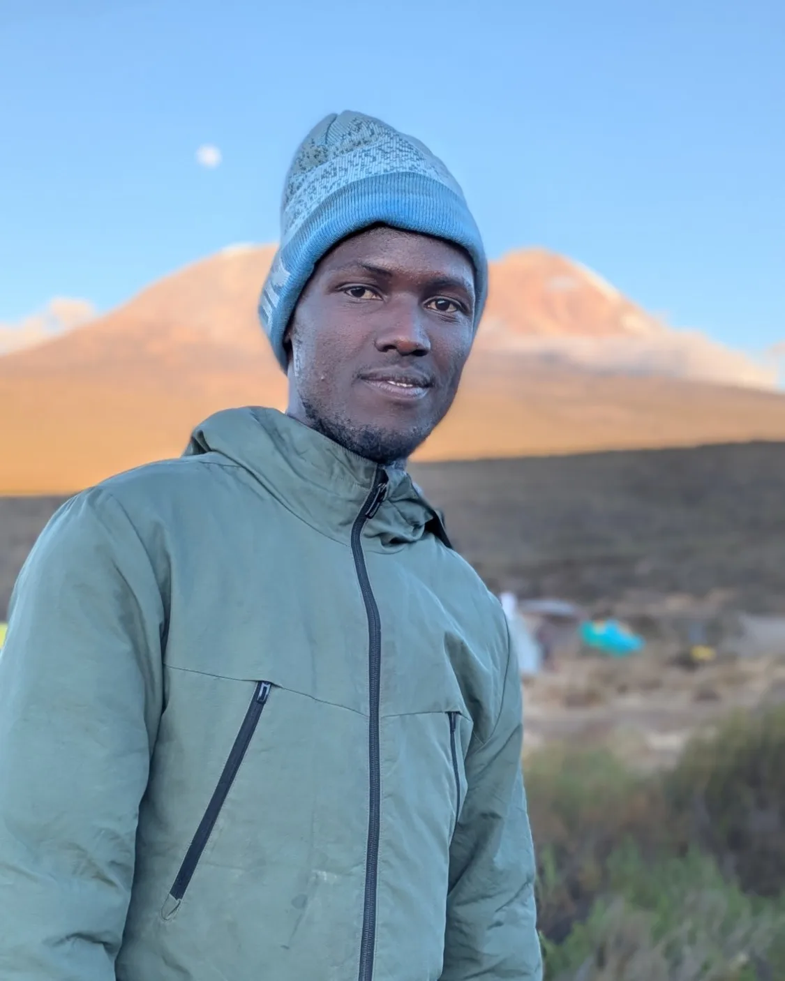 Peter Olomi at camp on Kilimanjaro at sunrise, with Kibo behind him