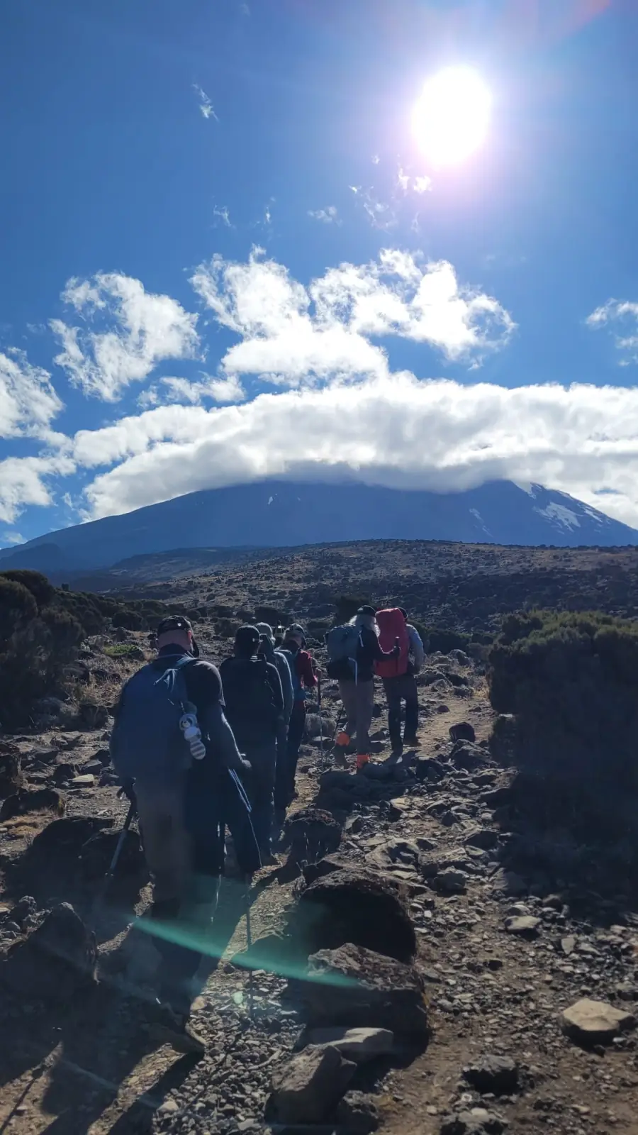 Trekkers on a rocky trail with the summit of Kibo under cloud behind them