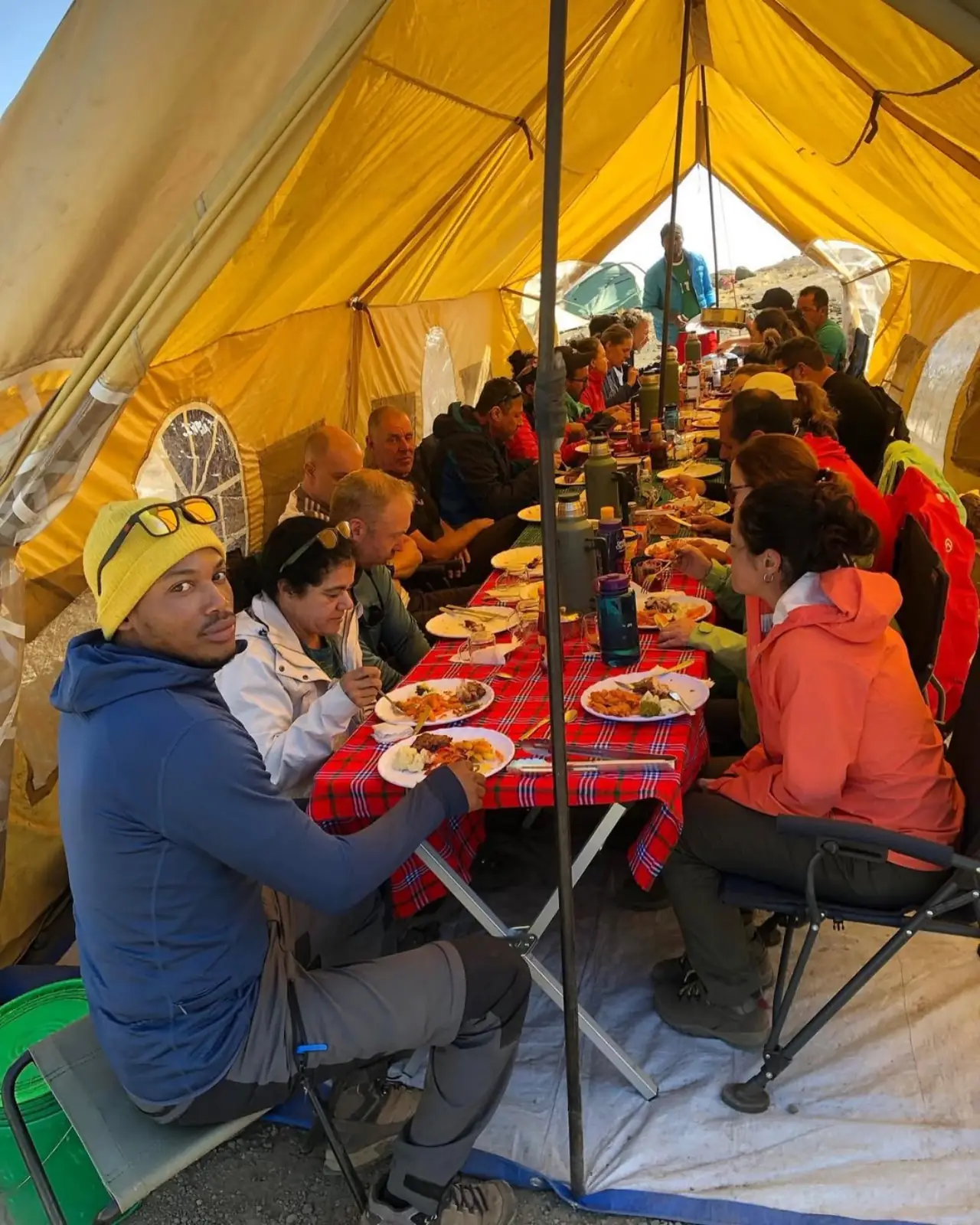 A group eating a hot meal together at a long table inside a yellow mess tent