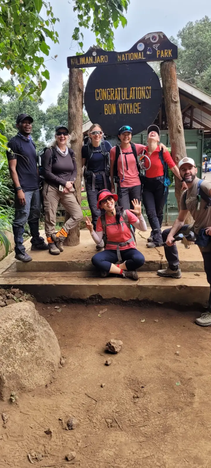 A group celebrating at the Kilimanjaro National Park gate sign after descending