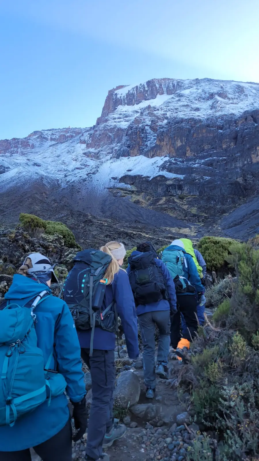 Trekkers ascending towards a snow-covered rock face high on the mountain