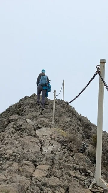 A trekker on the rocky summit ridge of Mount Meru beside the fixed chain handrail
